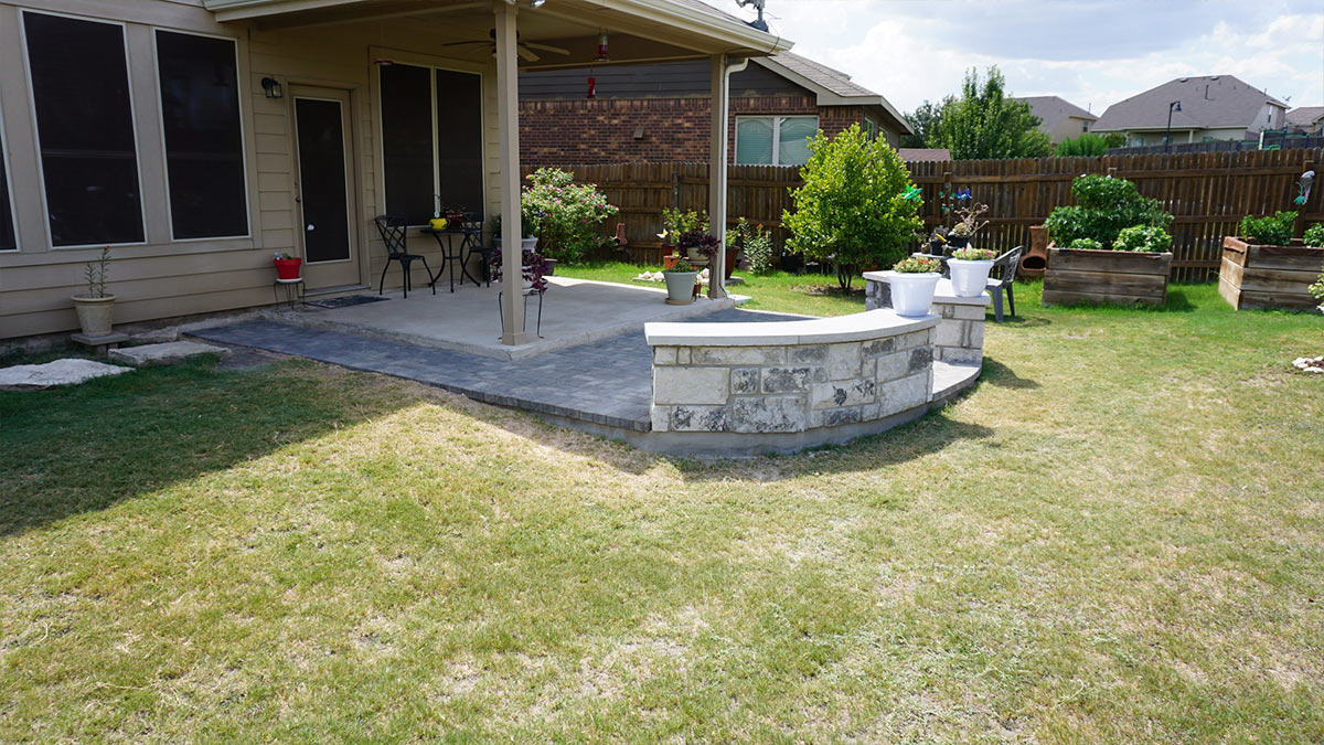 A backyard patio with a stone seating area, surrounded by planters and greenery, offering a relaxing outdoor space.