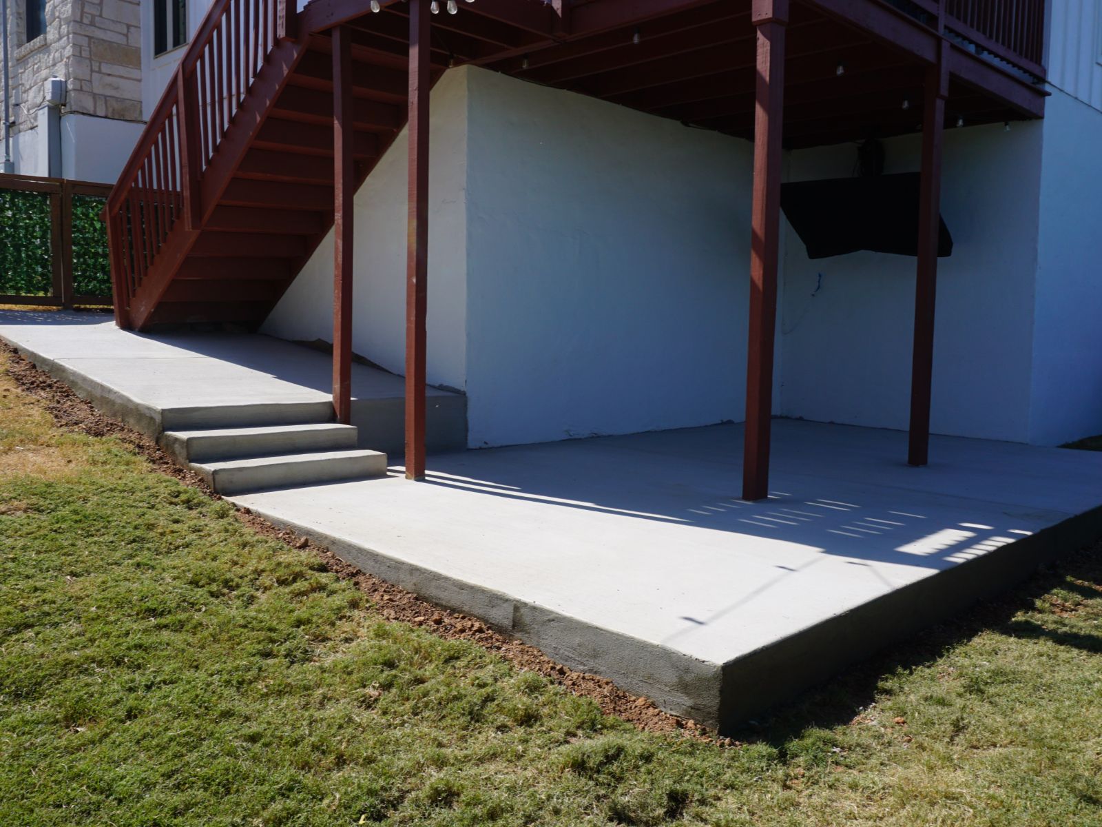 Concrete patio under deck stairs with lawn and fenced backyard