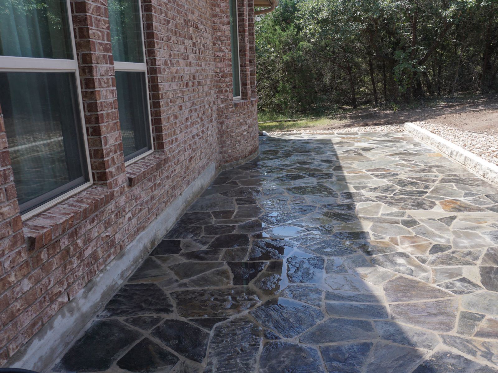 Flagstone patio beside brick house with stone retaining edge and surrounding trees