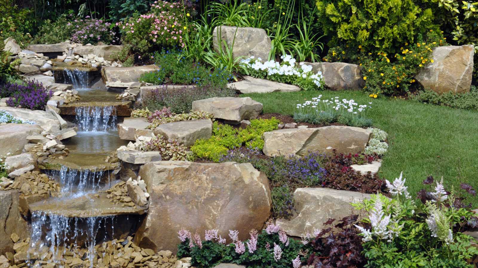 A serene garden with cascading water, vibrant flowers, and large stones, creating a picturesque natural landscape.