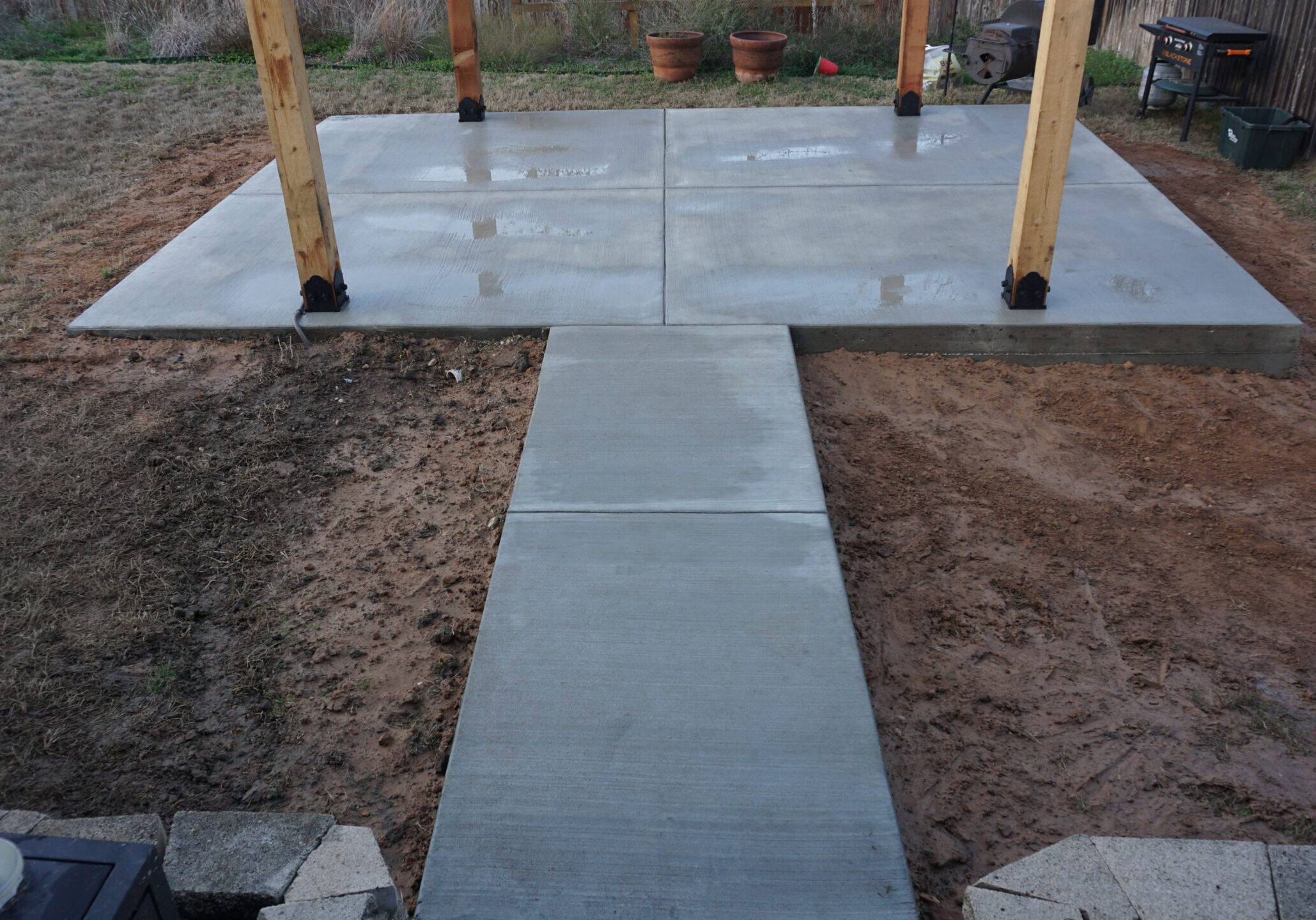 concrete pathway leading to concrete patio surrounded by dirt